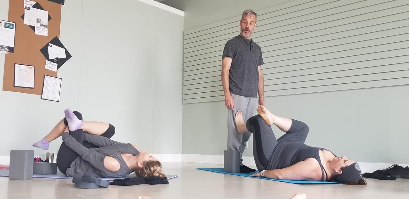 A man is standing next to two women doing yoga in a room.