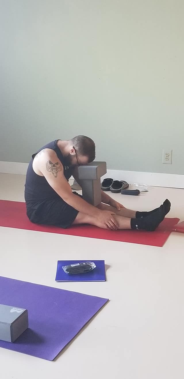 A man is sitting on a yoga mat stretching his legs.