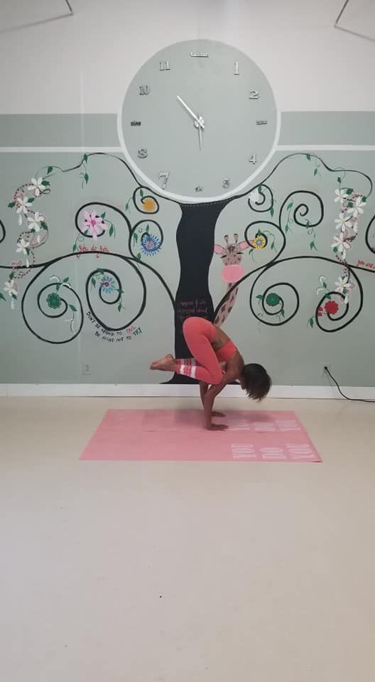 A person is doing a handstand on a yoga mat in front of a clock.