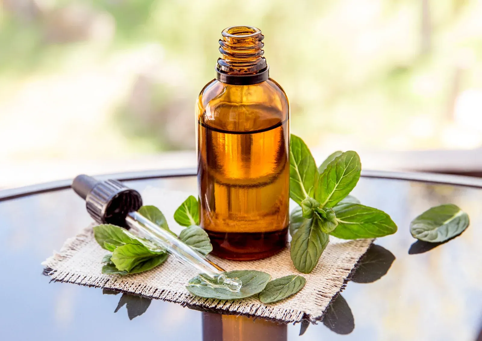 A bottle of essential oil with a dropper and mint leaves on a table.