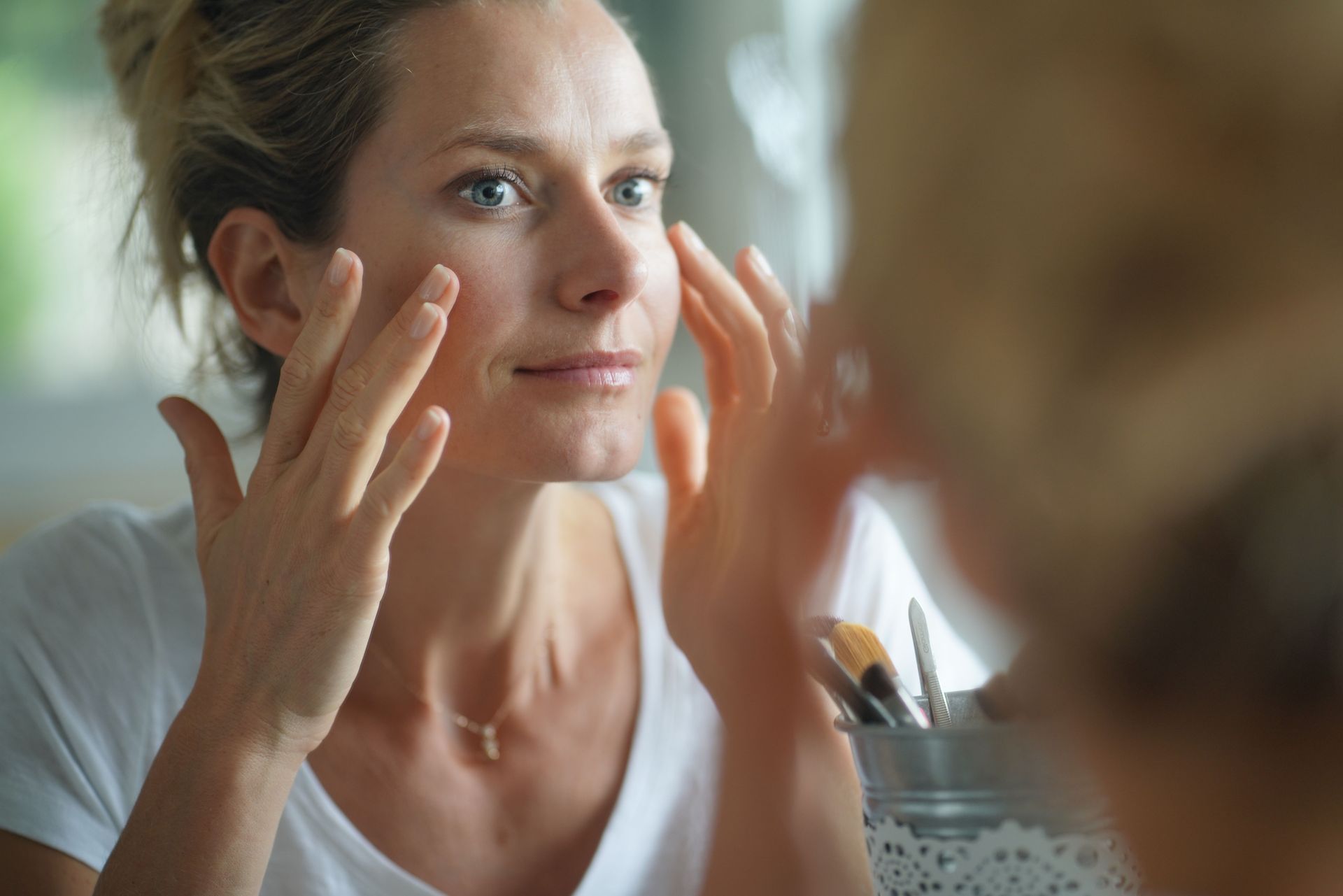 A woman is looking at her face in the mirror.