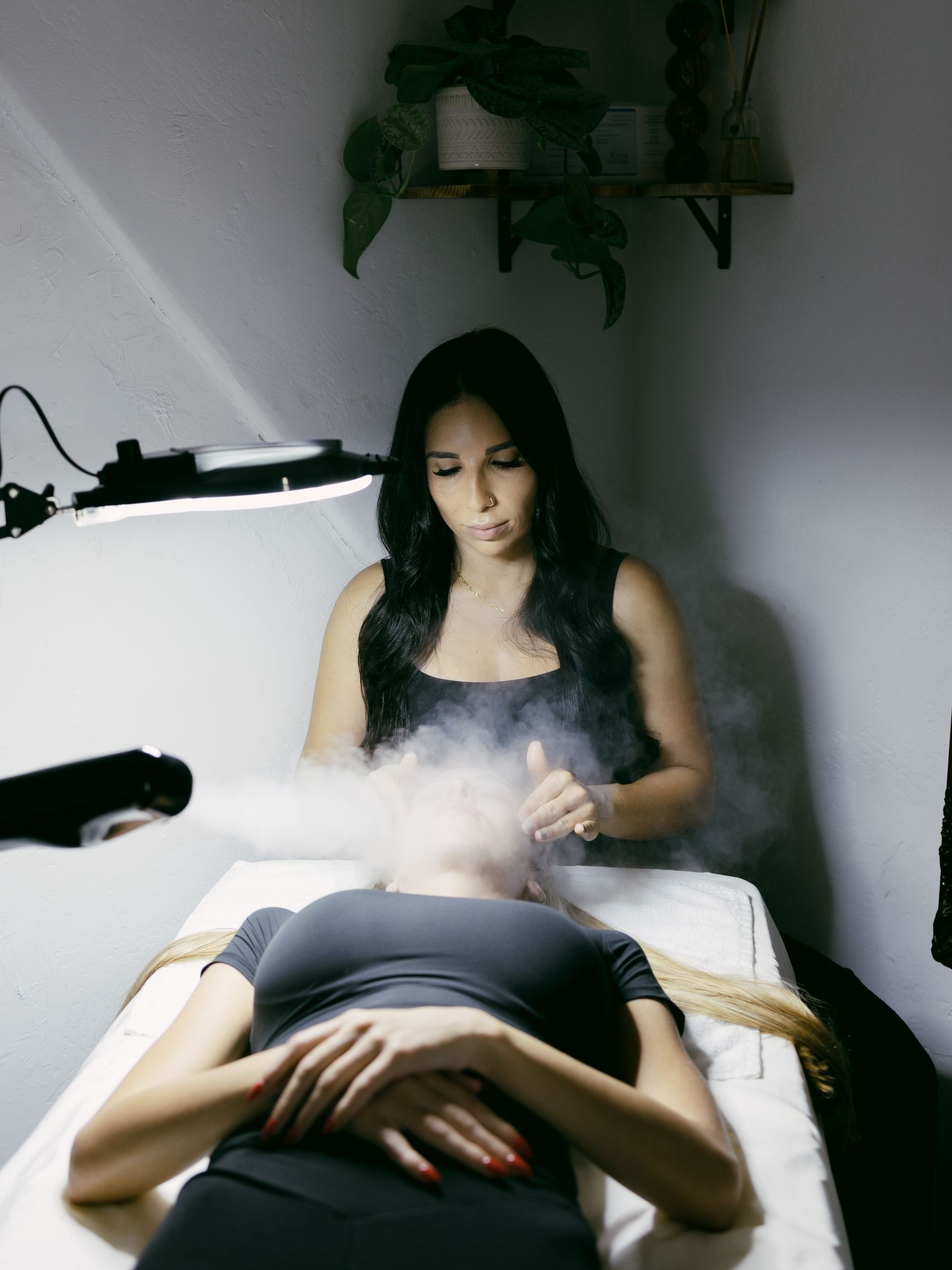 A woman is laying on a bed receiving a facial from an aesthetician