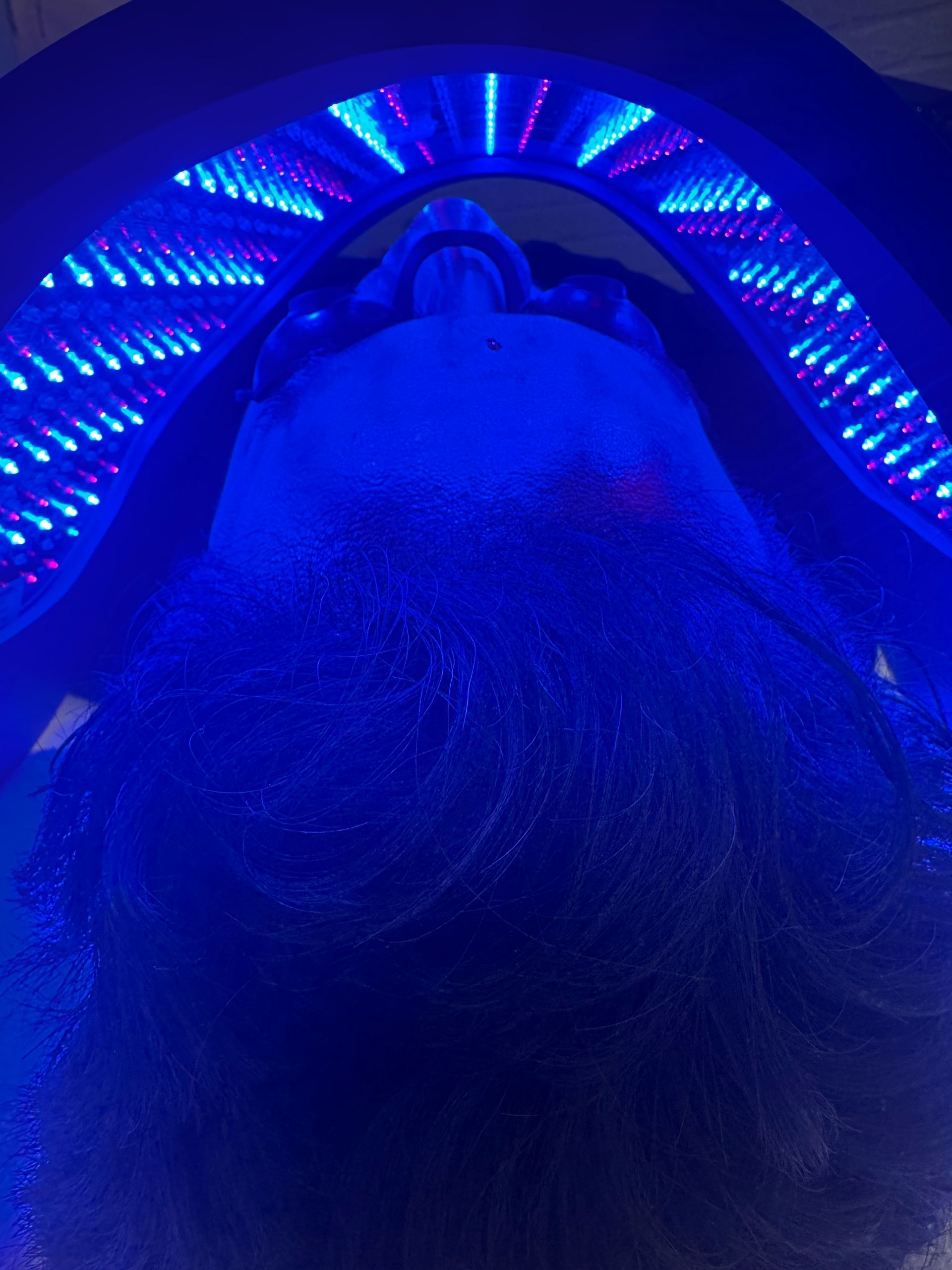 A person is holding an LED mask with blue lights before a skincare treatment