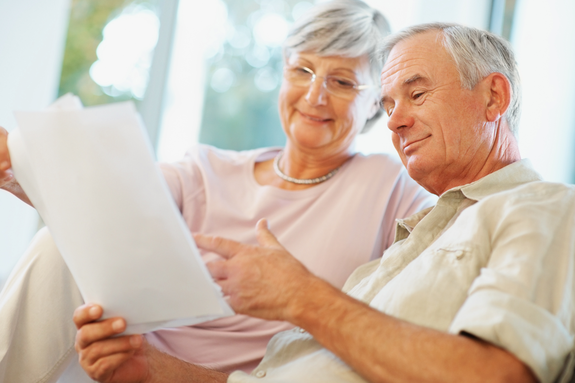 Older couple looking at paperwork, smiling. Indoor setting.
