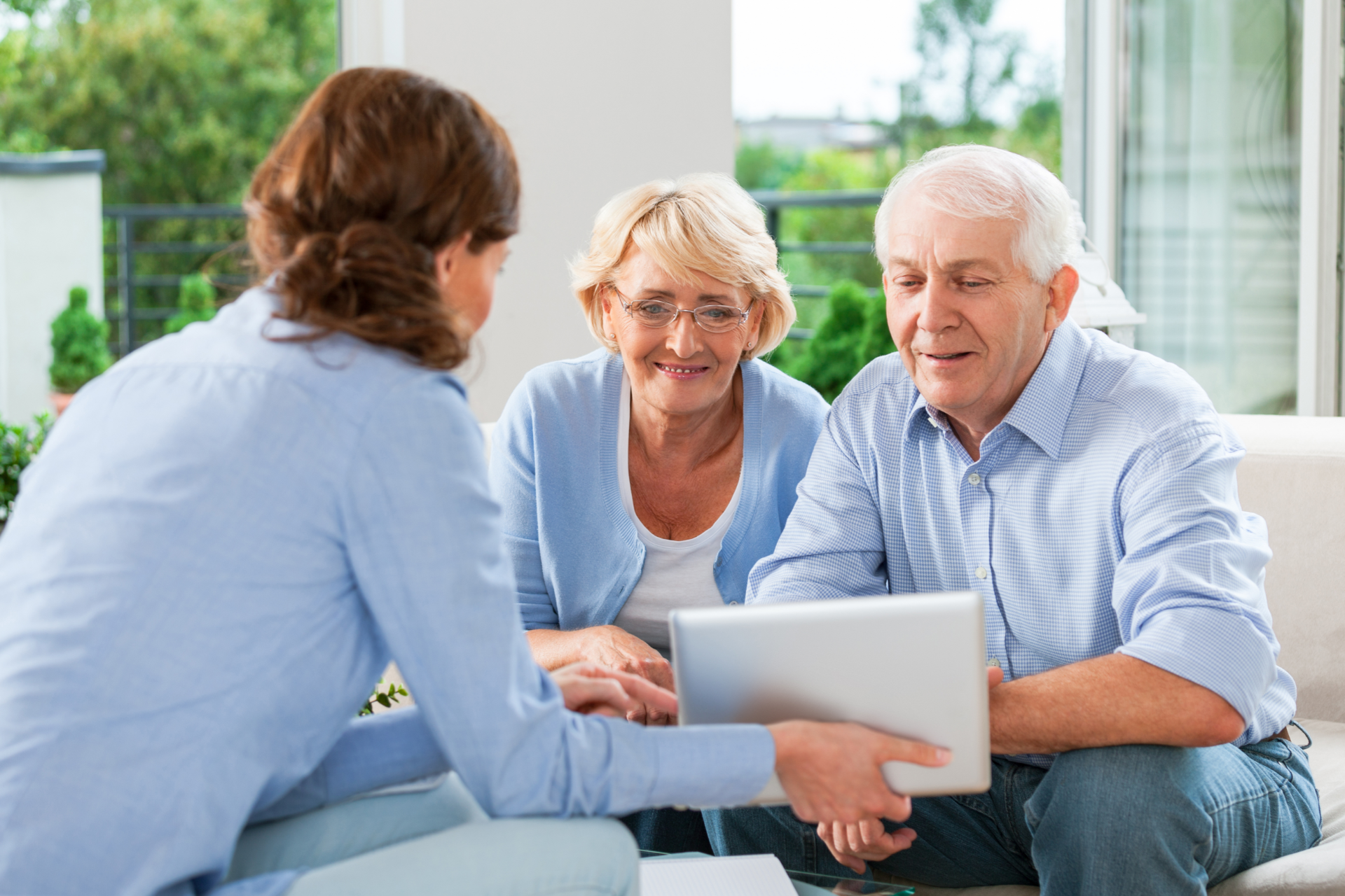 Woman shows a tablet to an older couple seated outdoors on a couch.