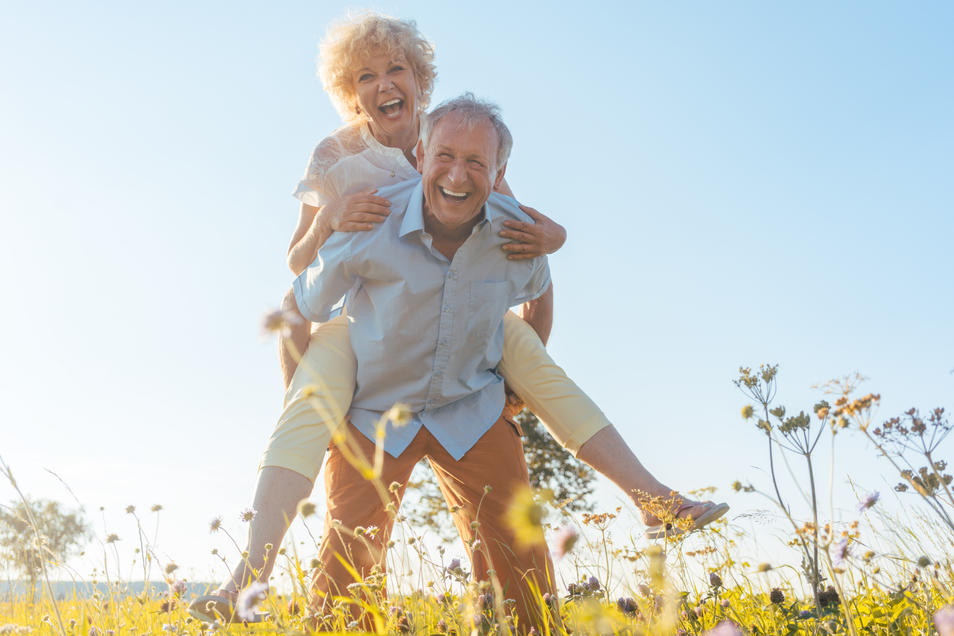 Smiling person giving another a piggyback ride in a sunny field.