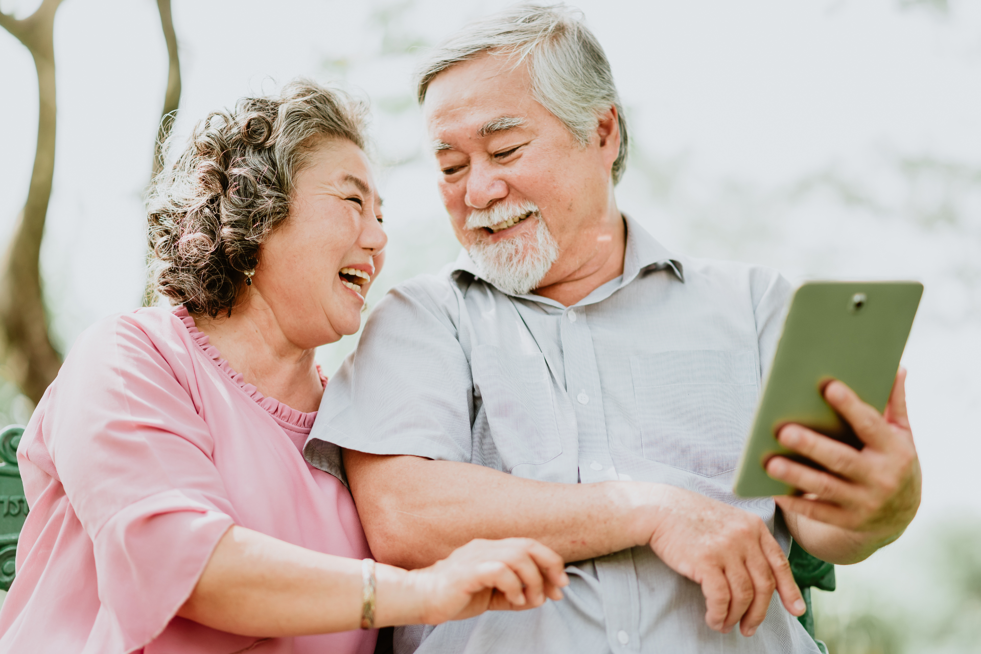 Senior couple looking at a tablet, smiling, outdoors.