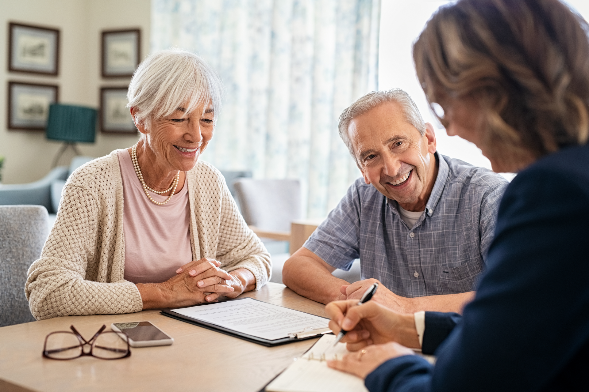 Senior couple smiling as person in suit signs document at table.