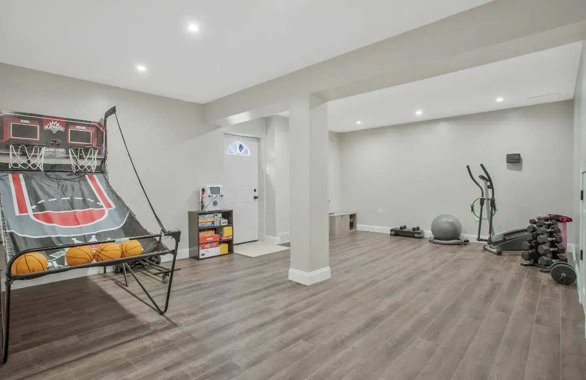 A basement with a basketball game , exercise equipment , and a basketball hoop.