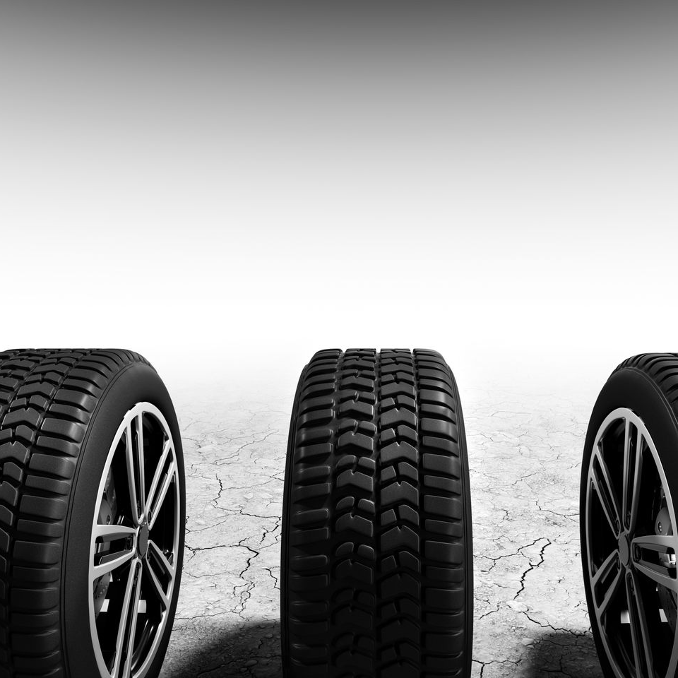 Three black car tires on a cracked surface, with a plain gray background.