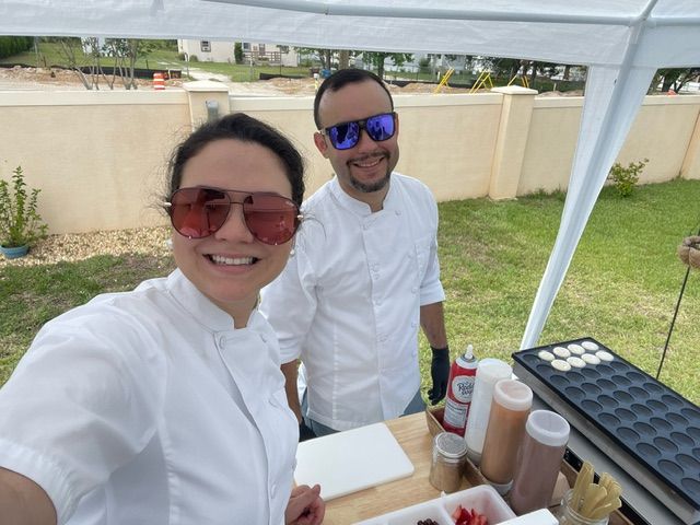 A table topped with plates of food and bowls of vegetables. Two personal chefs looking at the camera.