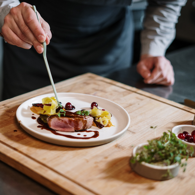 A person is preparing a plate of food on a wooden cutting board