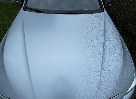 Zilveren motorkap met waterdruppels, reflecterend nat oppervlak.