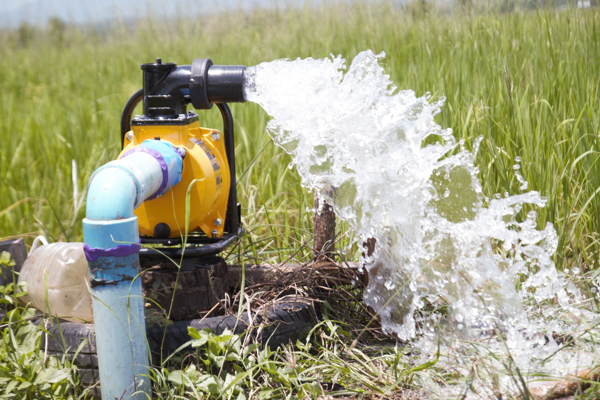 A yellow water pump in a grassy field discharging a strong stream of water into a channel.