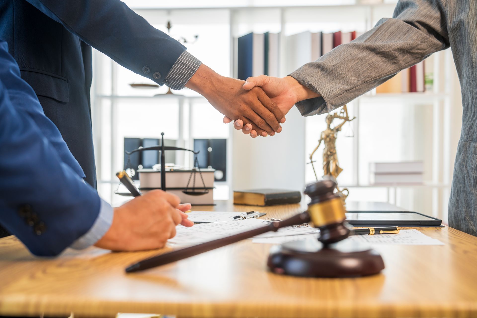 Two people shaking hands over a table with legal documents and a gavel.