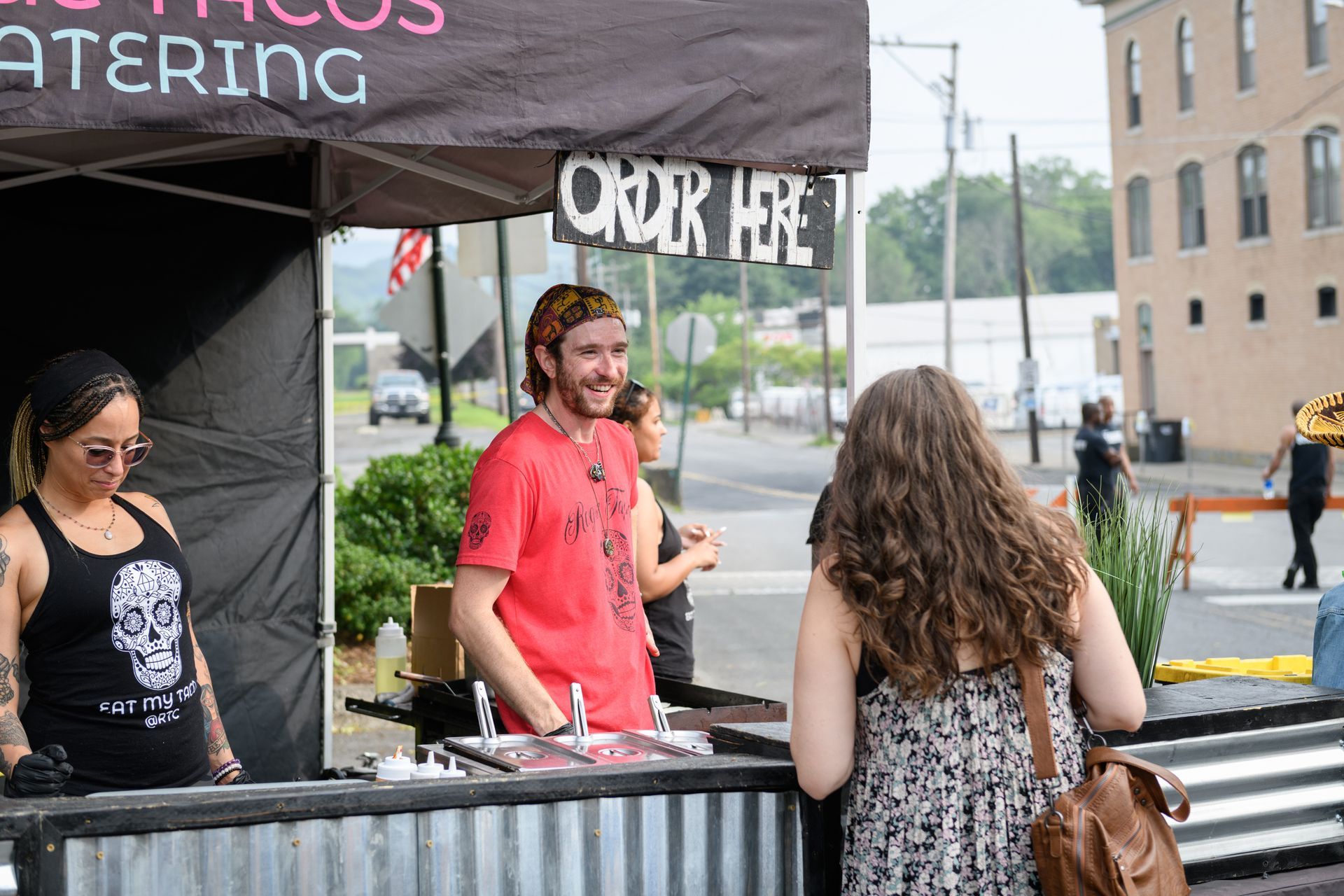 A man in a red shirt is standing in front of a tent with a sign that says order here.