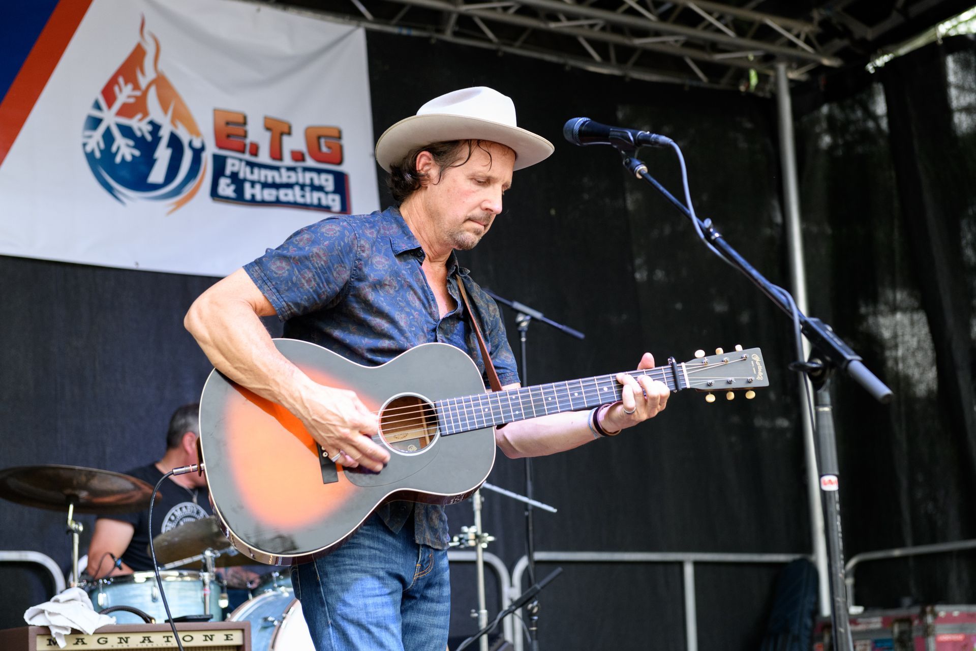 A man in a hat is playing a guitar in front of a banner that says e.t.g plumbing & heating