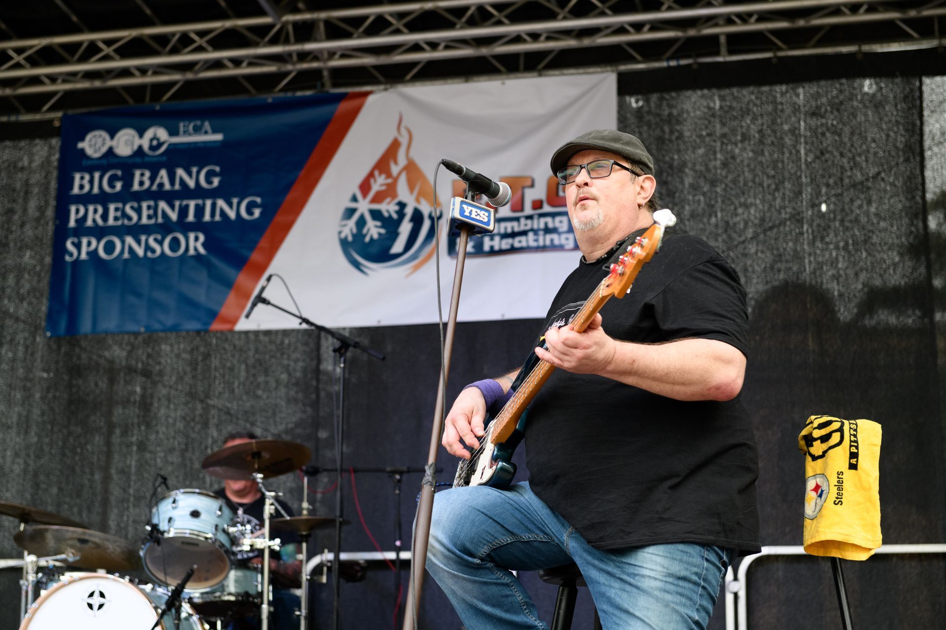 A man playing a guitar in front of a big bang presenting sponsor banner