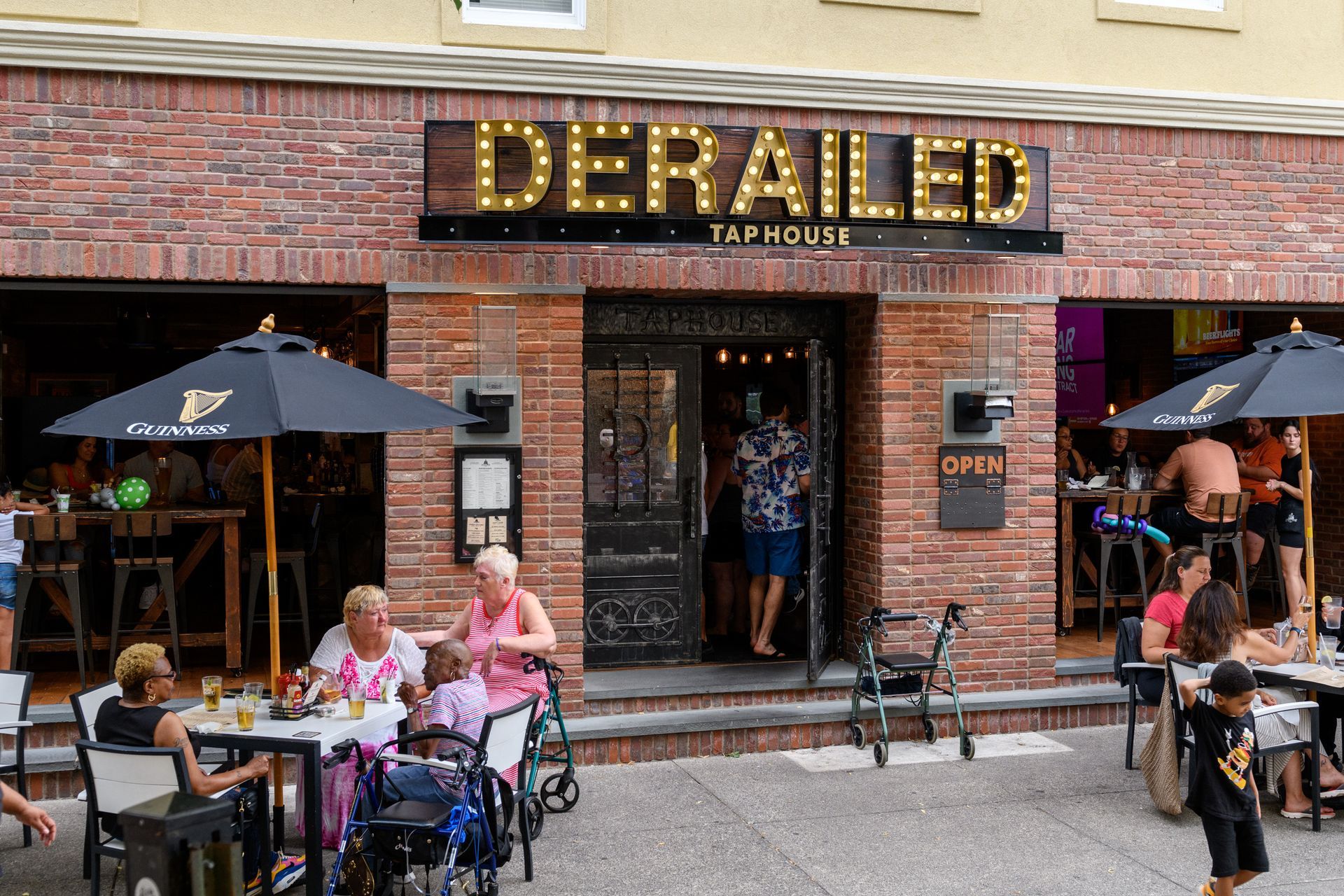 A group of people are sitting at tables outside of a restaurant called derailed.