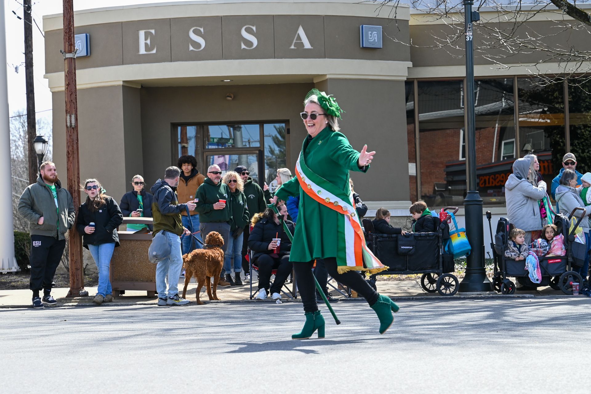 A woman in a green dress is walking down the street in front of a building.