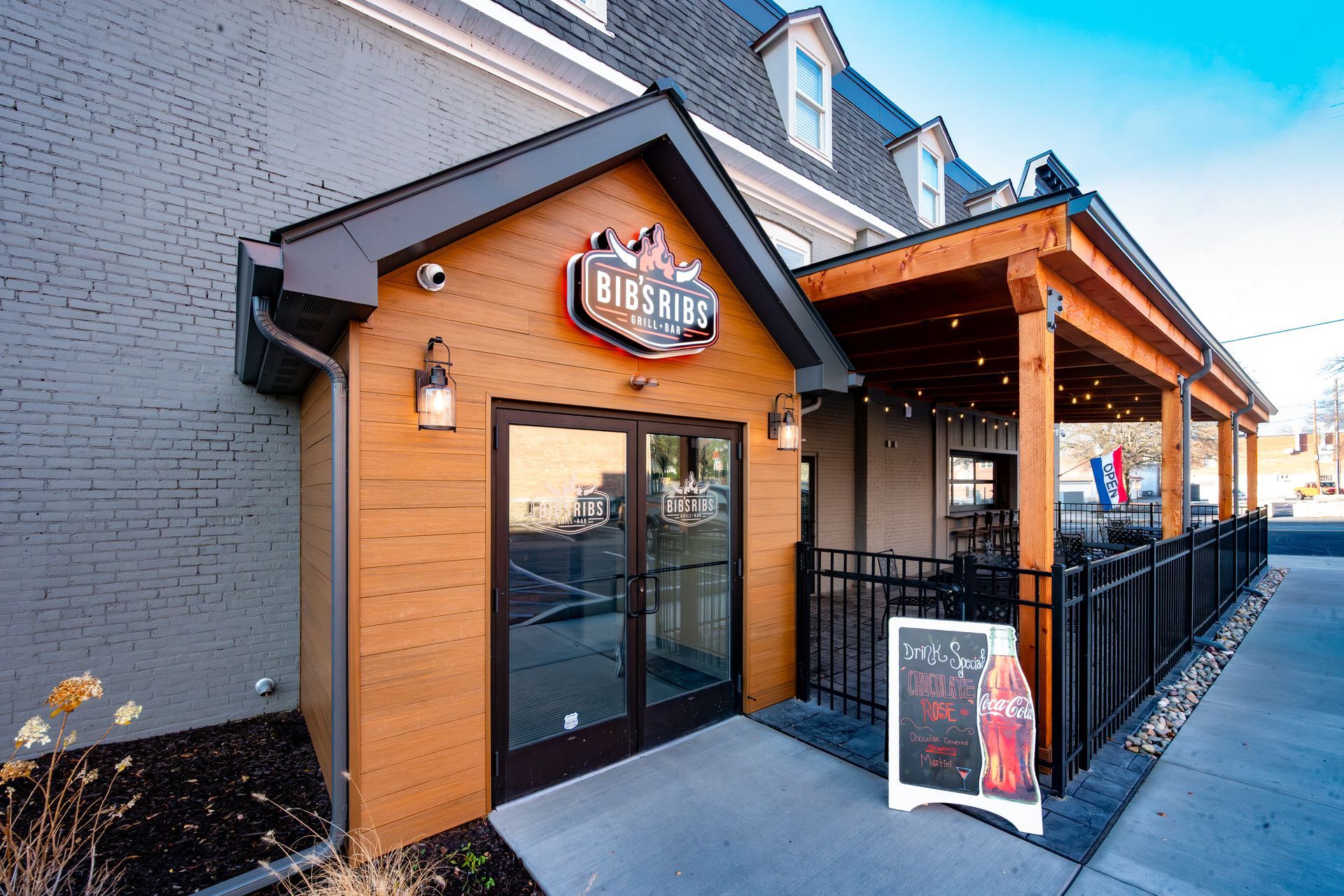 Restaurant entrance with wooden facade and covered outdoor seating. Sign above door.