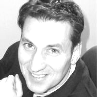 Man smiling, looking towards the camera, wearing a dark burgundy shirt with a white collar.