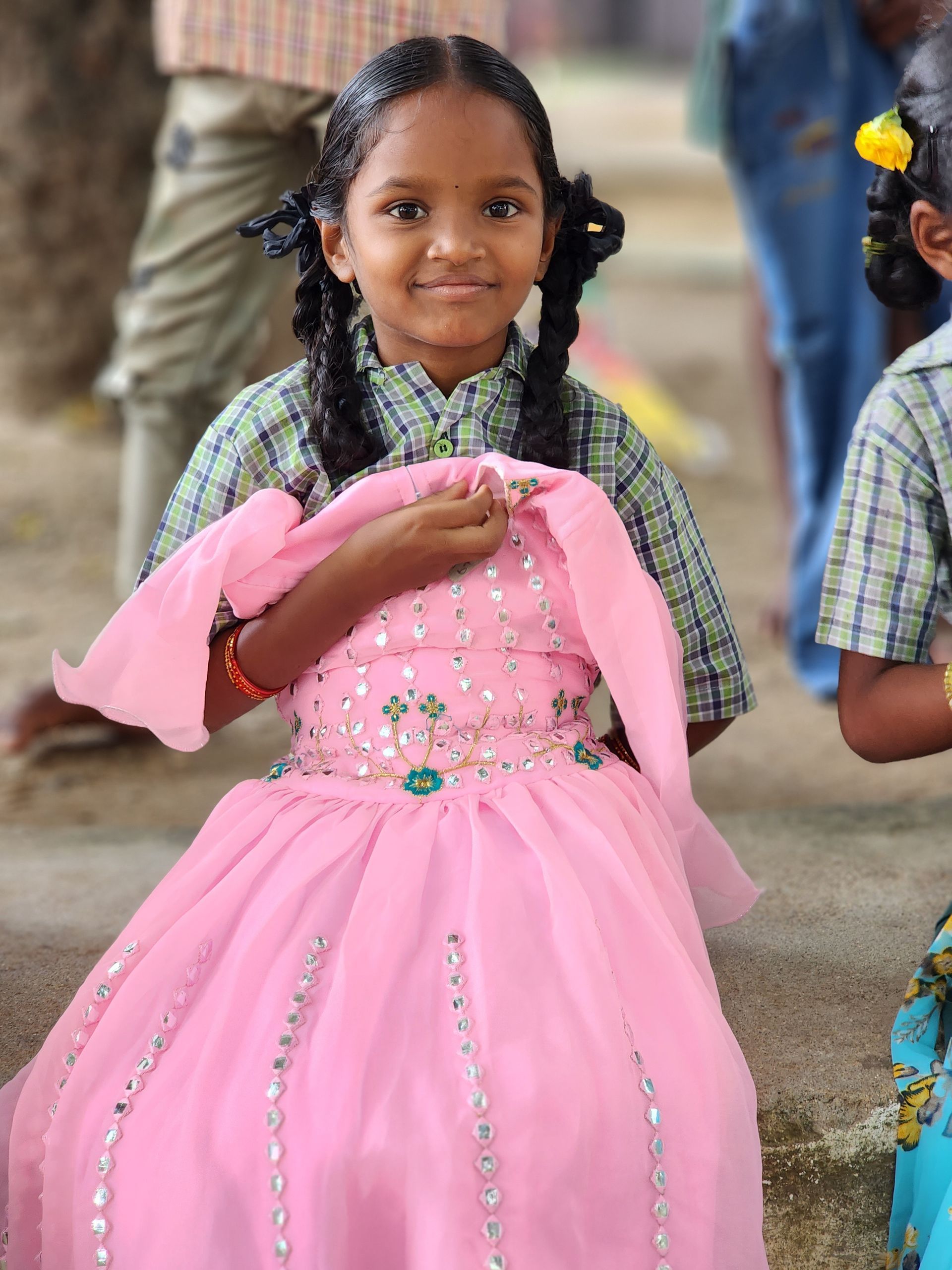 A little girl in a pink dress is sitting on the ground holding a pink cloth.