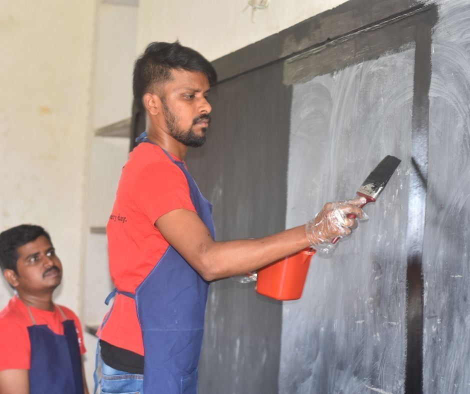 An employee painting a school blackboard as part of CSR activity