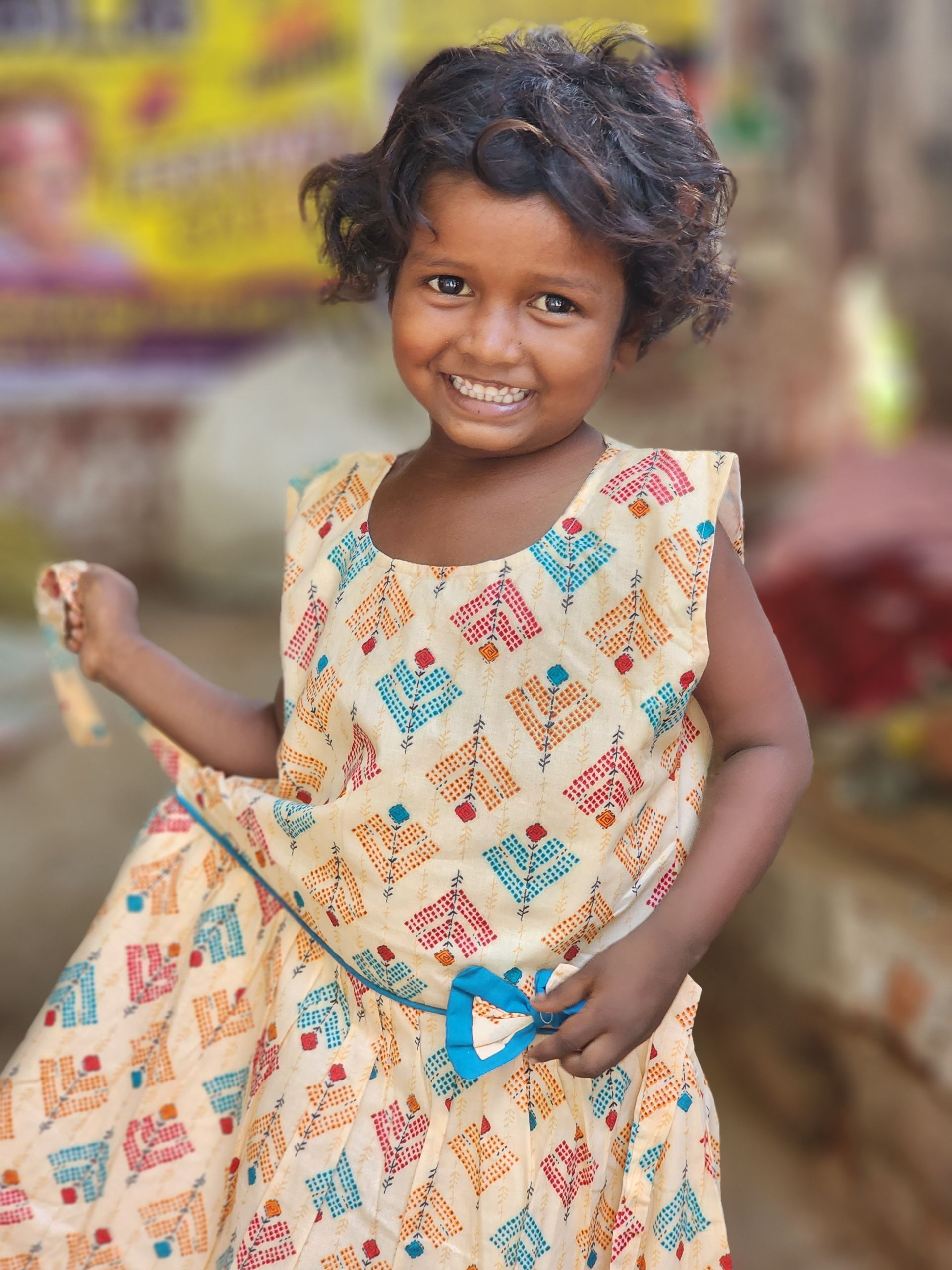 A little girl in a dress is smiling and holding a toy.