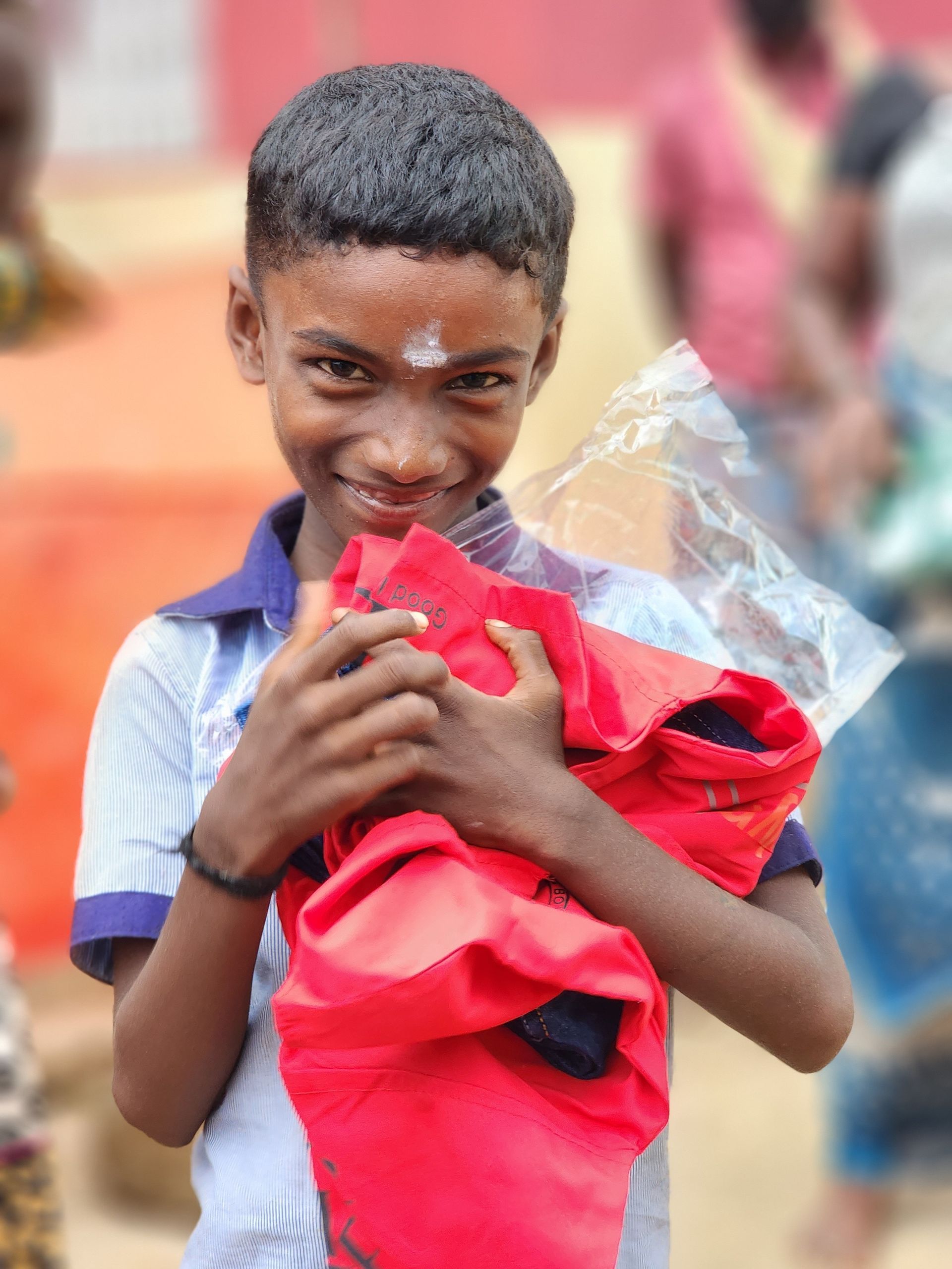 A young boy is holding a red shirt in his hands and smiling.