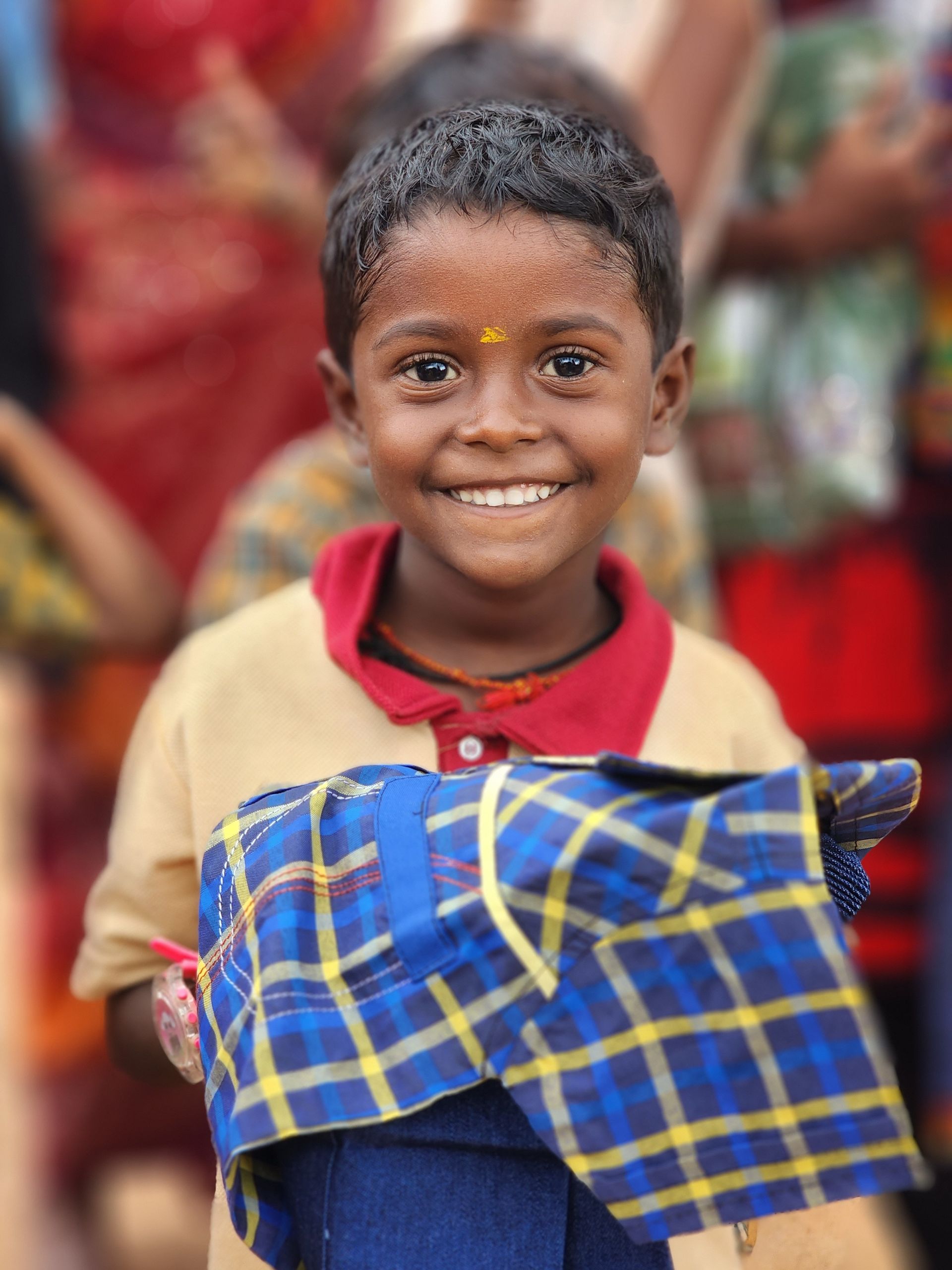 A young boy is holding a plaid shirt and smiling for the camera.