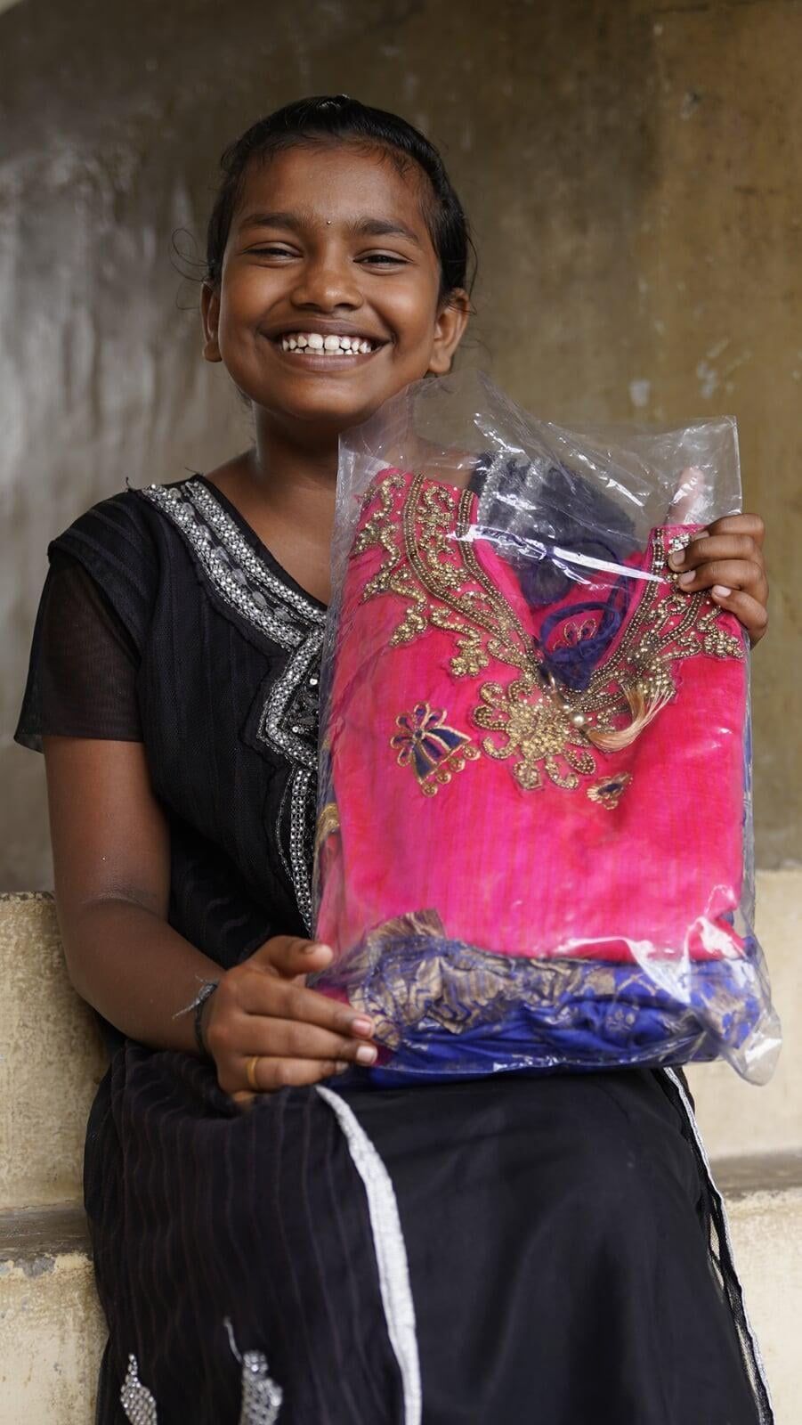A young girl is holding a pink dress in a plastic bag.