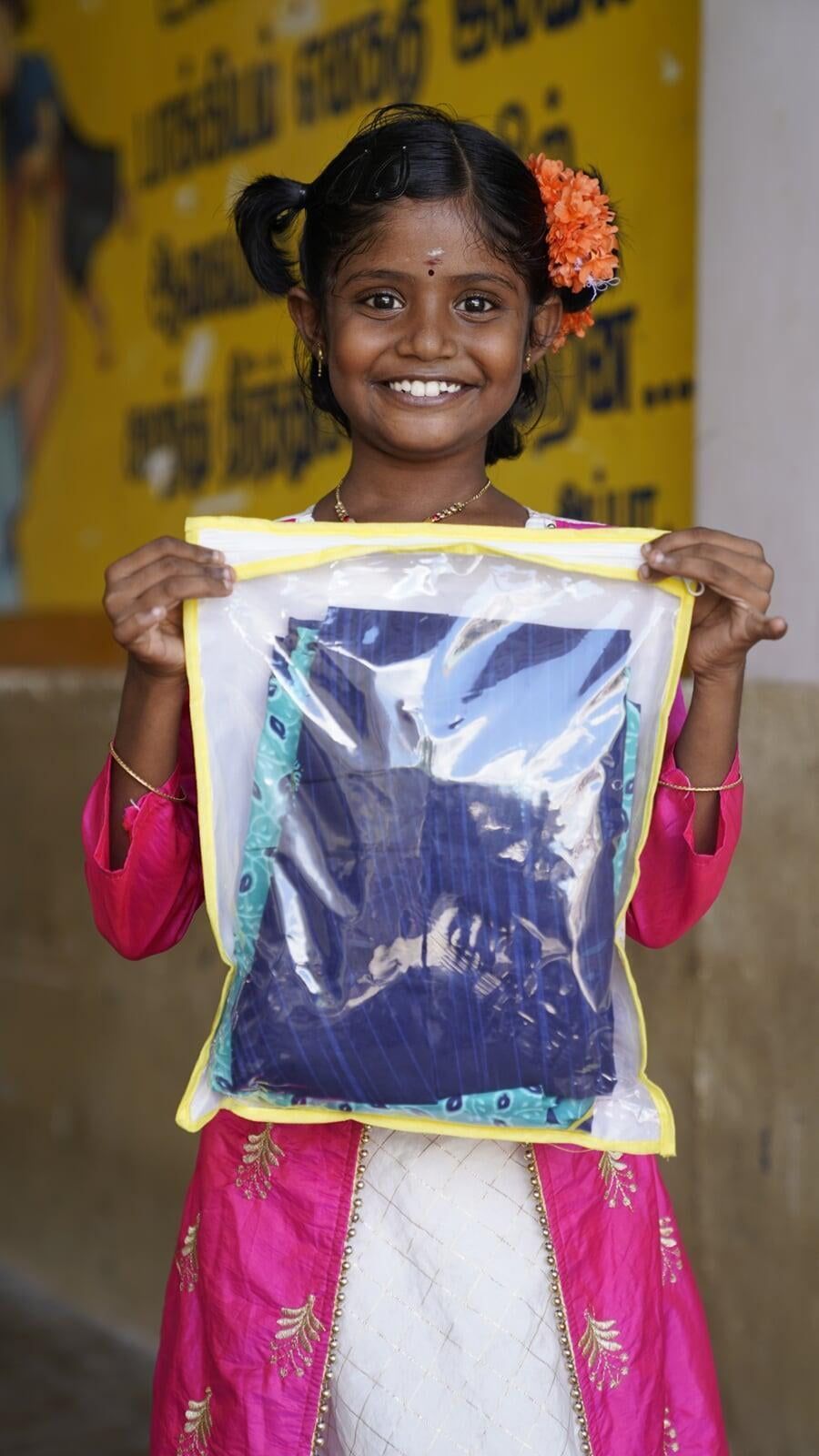 A little girl in a pink dress is holding a plastic bag with a picture on it.