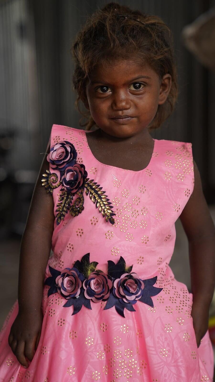 A little girl is wearing a pink dress with flowers on it.