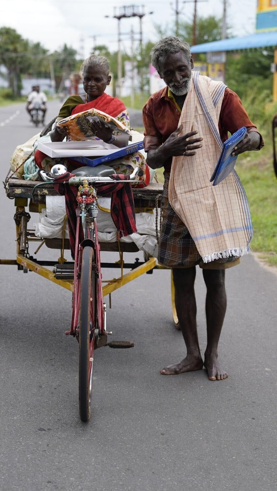 A man is standing next to a rickshaw pulled by a bicycle.