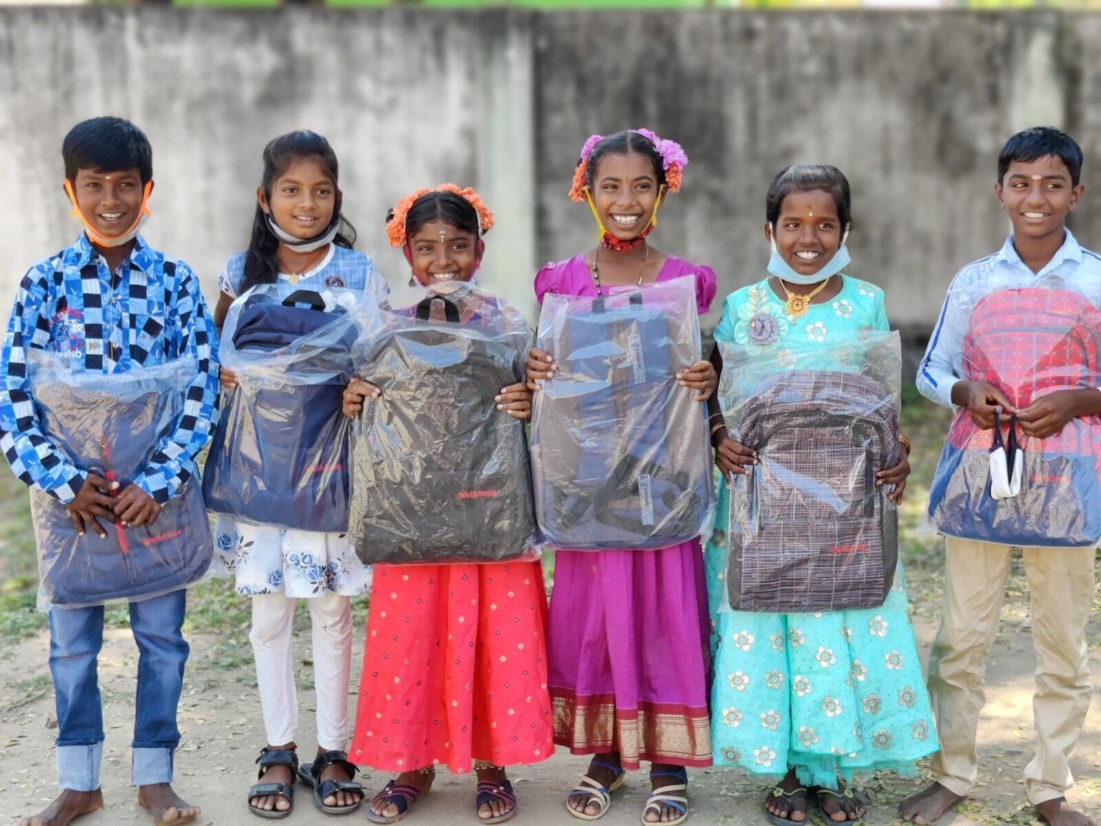A group of children are standing next to each other holding bags of clothes.