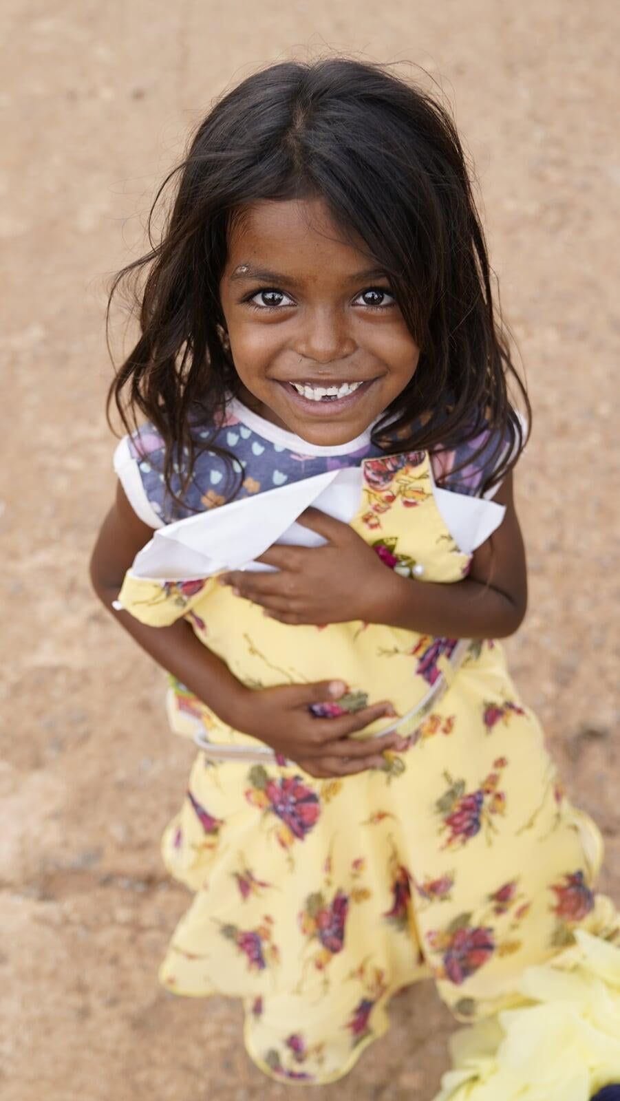 A little girl in a yellow dress is holding a blanket and smiling.