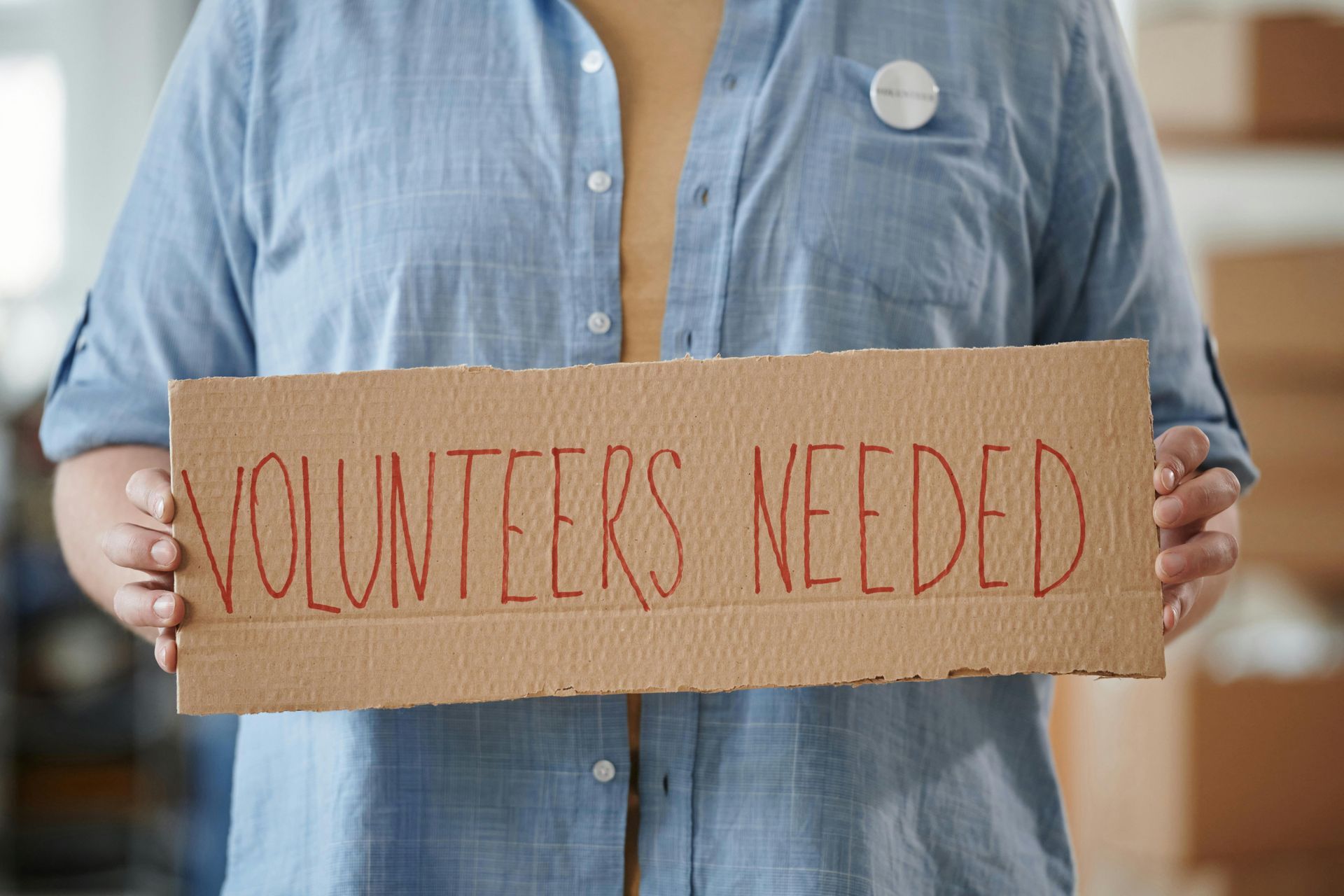 A woman is holding a cardboard sign that says `` volunteers needed ''.