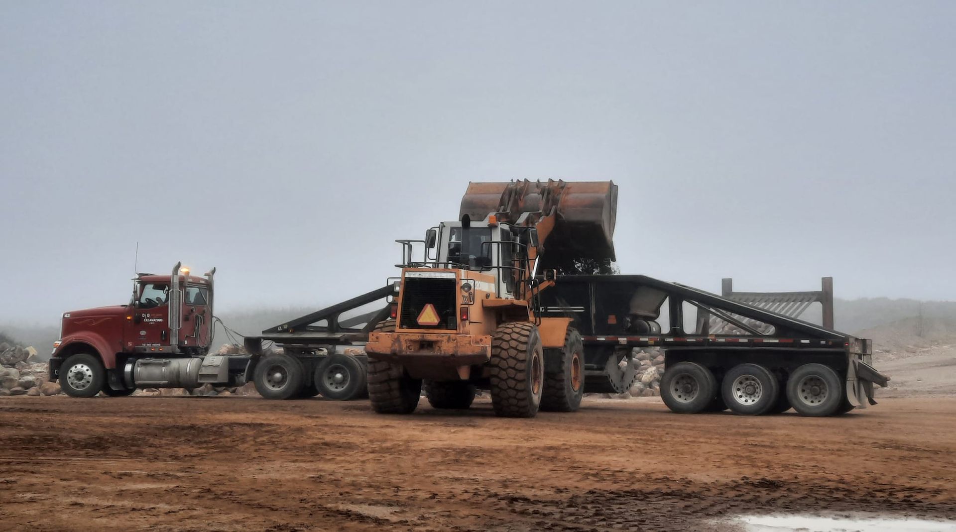 A red semi truck is towing a bulldozer on a dirt road.
