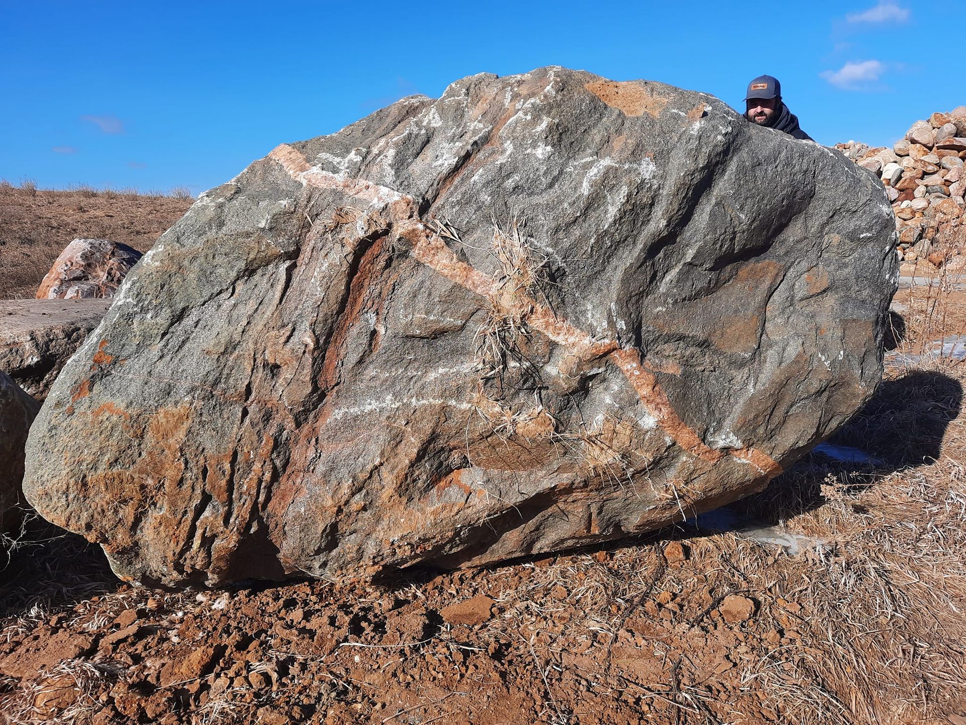 A man is standing next to a large rock in the dirt.