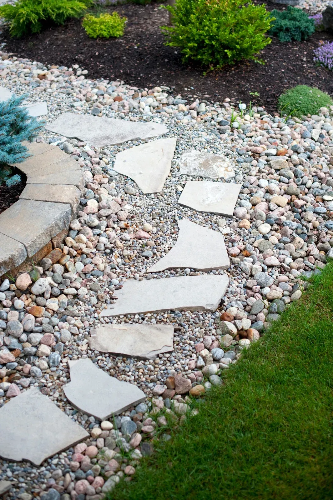 A stone walkway in a garden surrounded by rocks and grass.