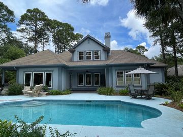 Blue house with pool and patio furniture. Overcast sky.