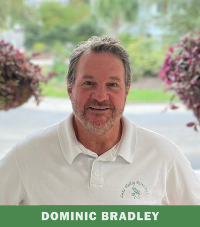 A man with a beard is wearing a white polo shirt and smiling.