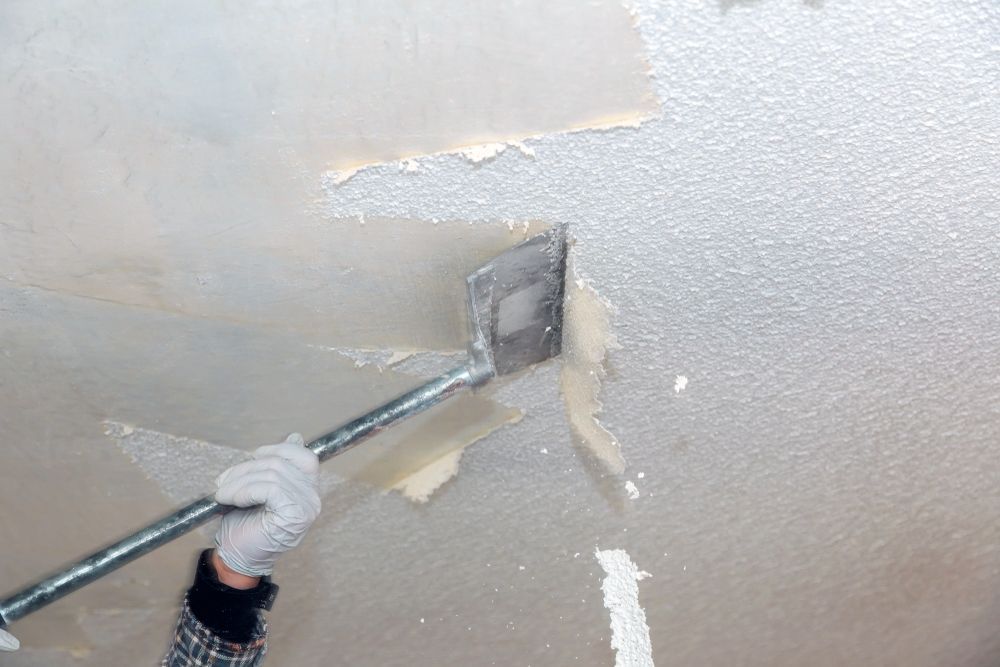 A person is using a spatula to remove wallpaper from a ceiling.