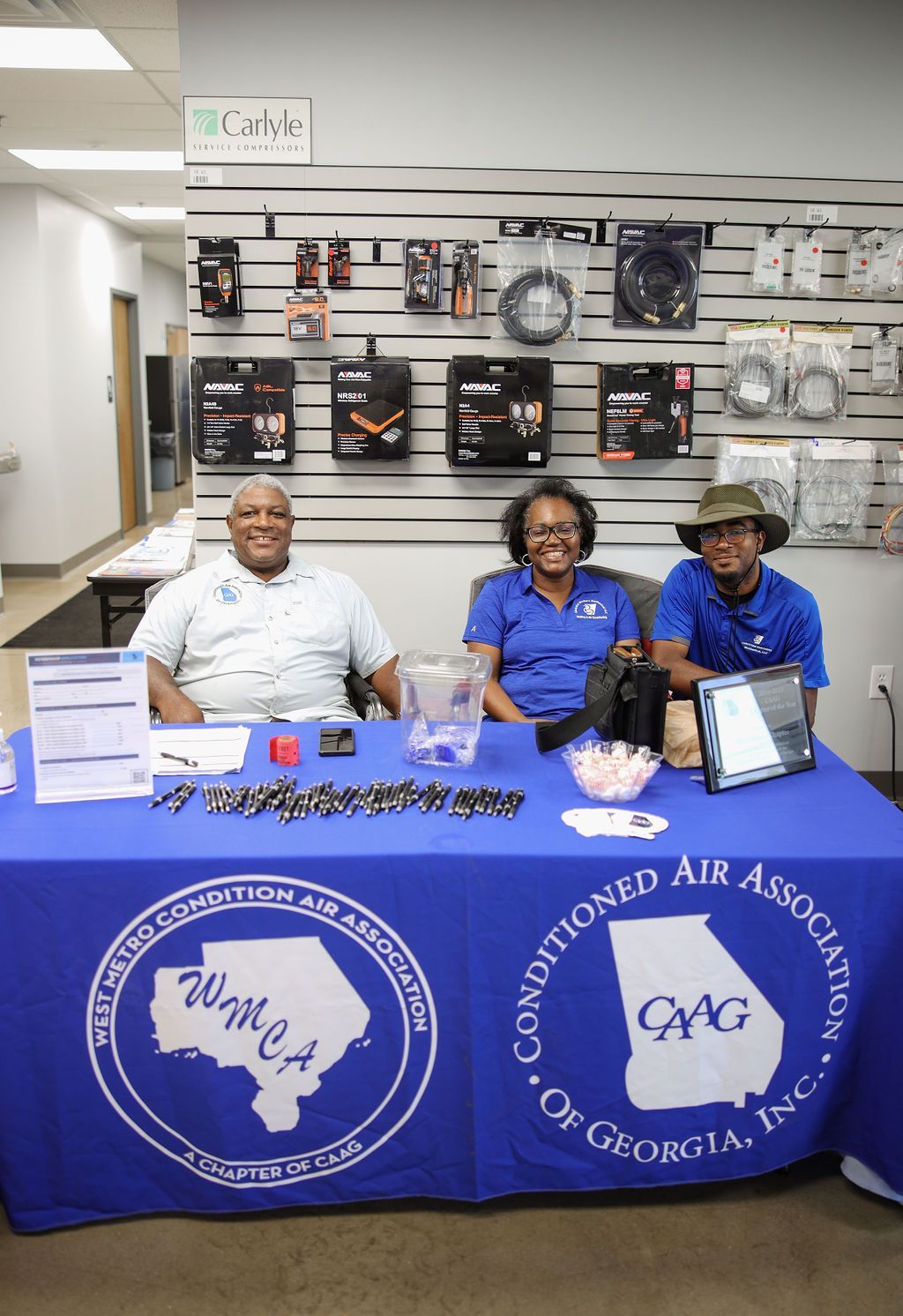 Three people are sitting at a table with a blue table cloth that says conditioning air association of georgia inc.