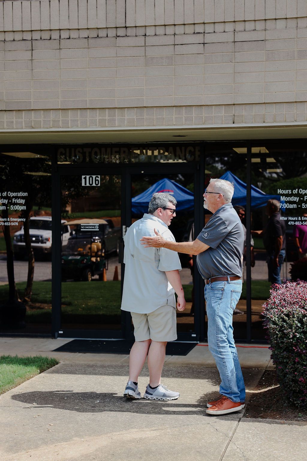 Two men are standing in front of a building talking to each other.