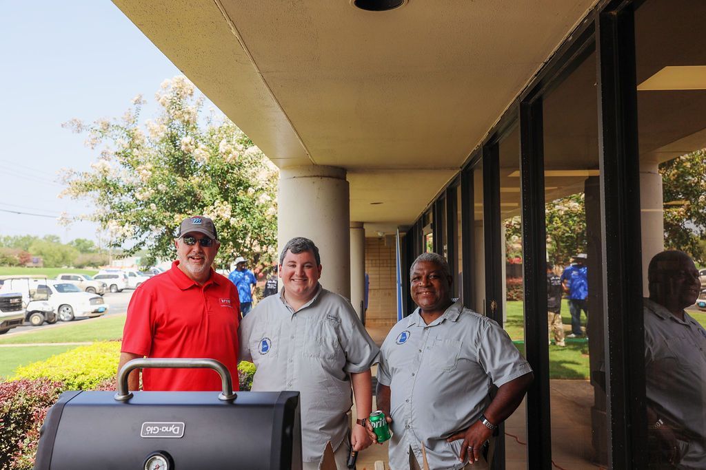 Three men are standing in front of a grill.