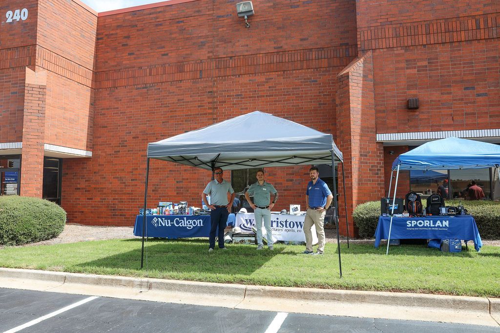 A group of people standing under a tent in front of a brick building.