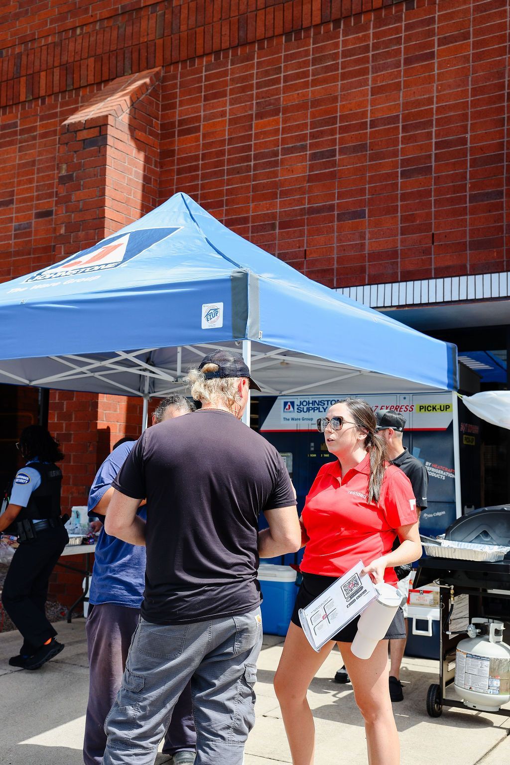 A group of people are standing under a blue tent in front of a brick building.