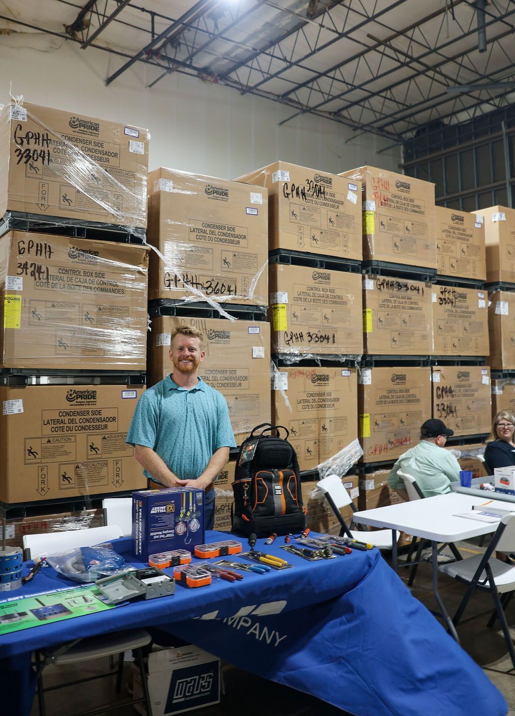 A man is standing in front of a table in a warehouse filled with boxes.